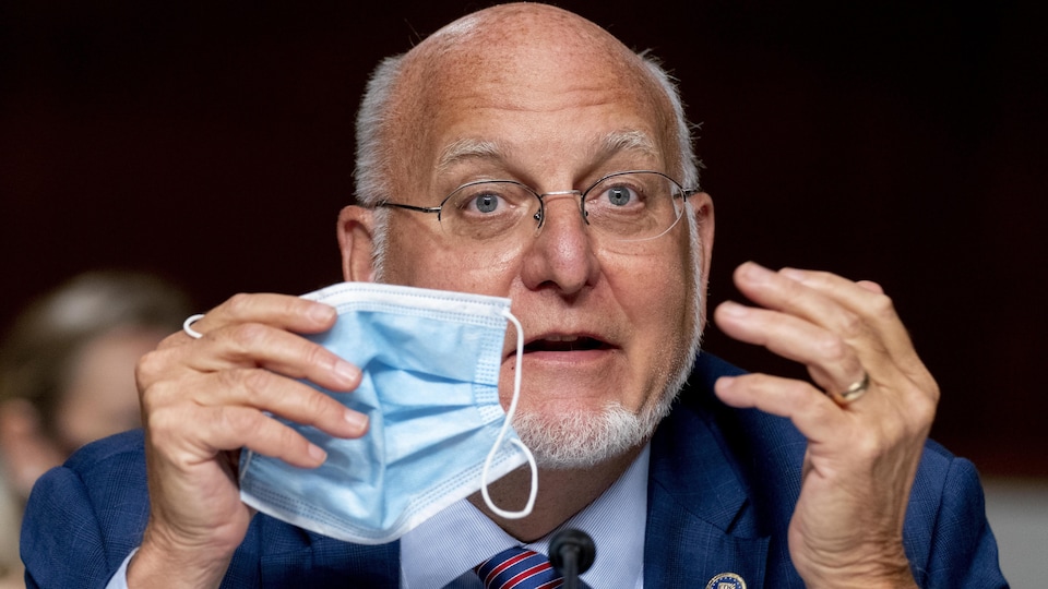 Le Dr Robert Redfield s'adresse aux sénateurs en tenant un masque à la hauteur de son visage.