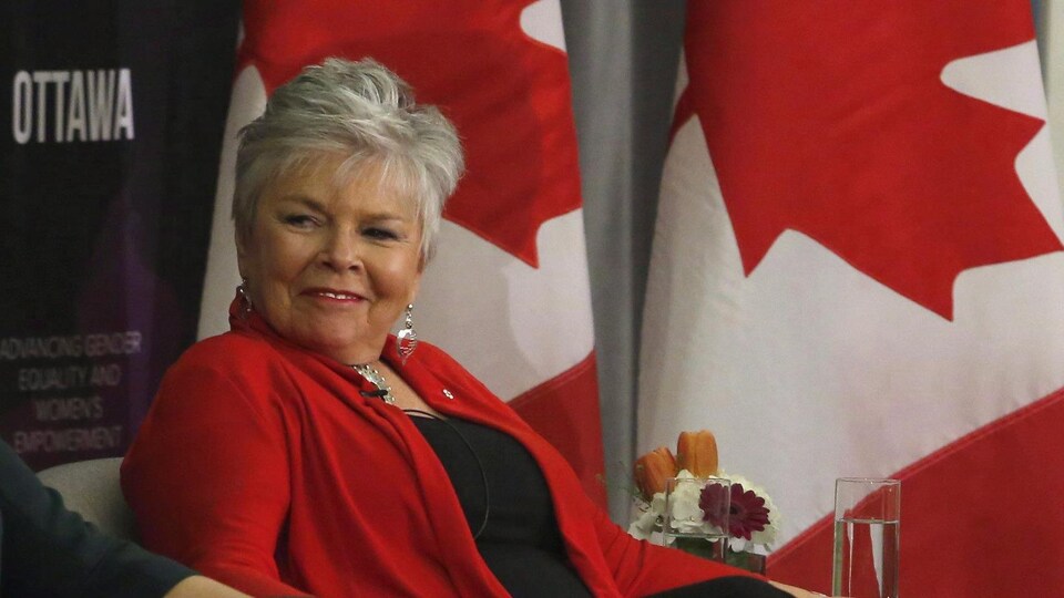 Roberta Jamieson est assise devant des drapeaux du Canada.