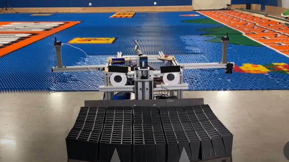 Un robot avec des yeux en plastique sourit devant une fresque de dominos à l'effigie du jeu vidéo Super Mario Bros.