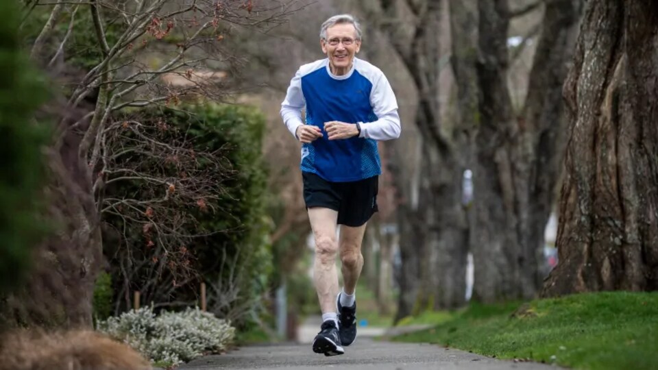 Rod Waterlow en train de courir sur un trottoir entouré d'arbres.