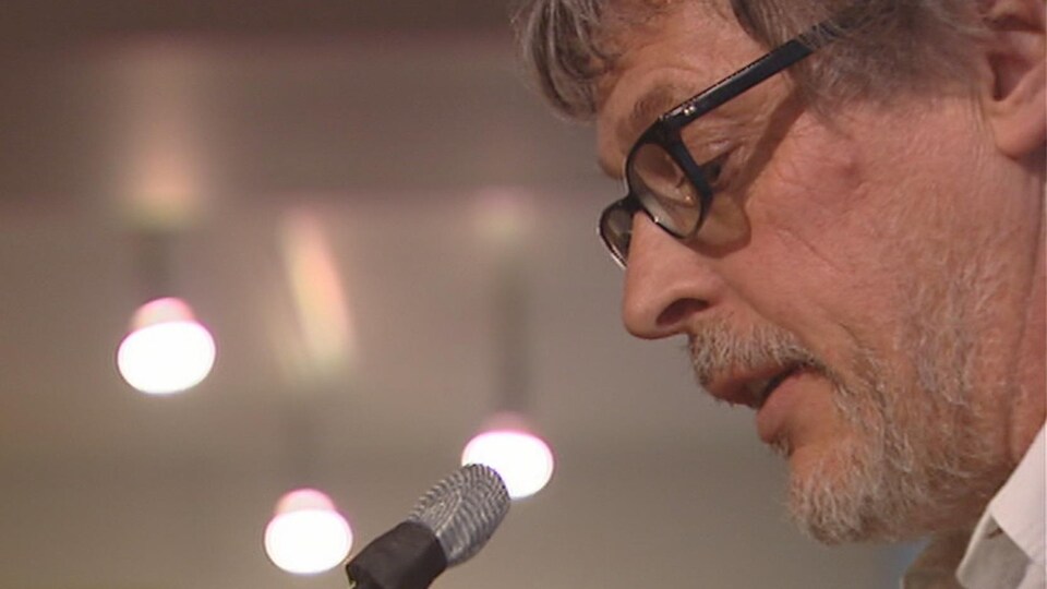 L'artiste Rodney Graham parle devant un micro.