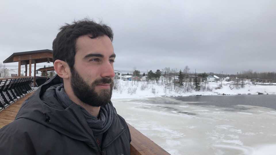 Rodrigue Turgeon, portant un manteau noir, regarde vers la rivière sous un ciel nuageux et sombre.