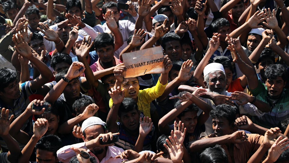 Une foule d'hommes dont la plupart ont les bras levés. Un de ceux-ci portent une pancarte portant l'inscription « We want justice» (Nous voulons que justice soit faite».