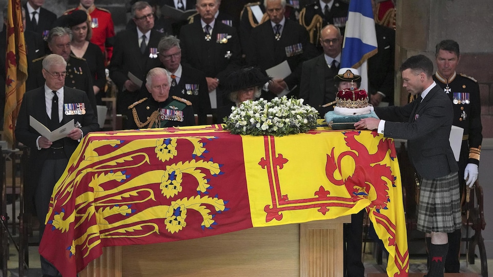 Le cercueil de la reine est sous un drapeau et un homme dépose dessus une couronne en or massif.