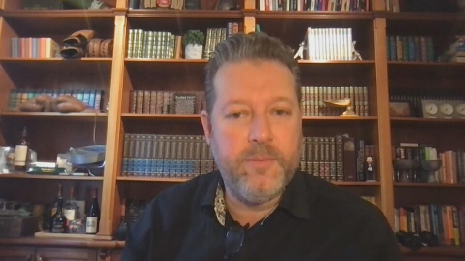 Un homme devant des étagères avec des livres.