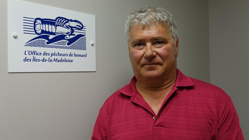 Rolland Turbide photographié devant une pancarte de l'Office des pêcheurs de homard des Îles-de-la-Madeleine.