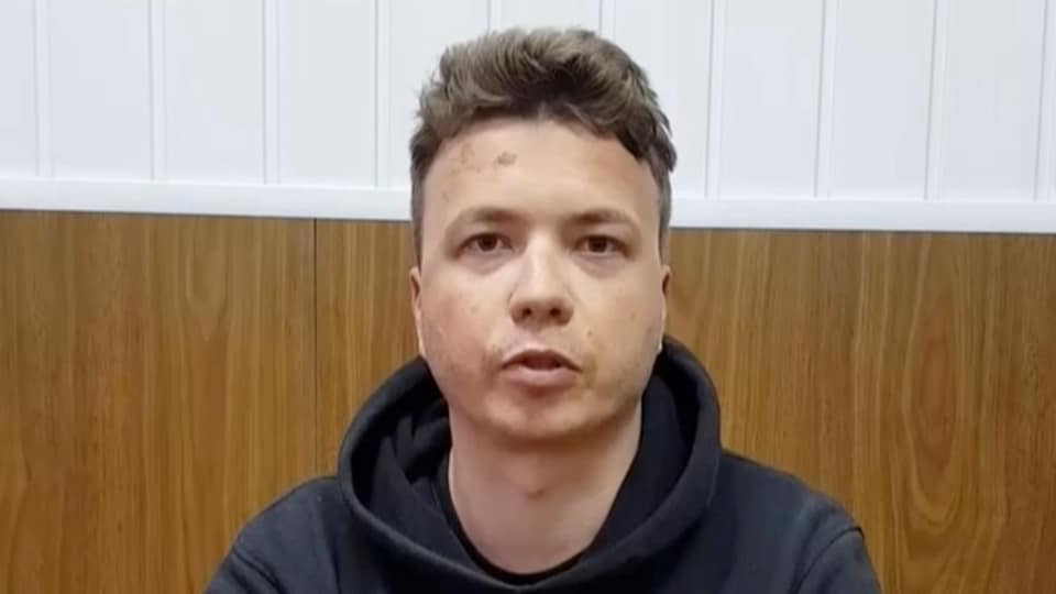 Un homme portant un coton ouaté est assis derrière une table, les mains croisées devant lui.