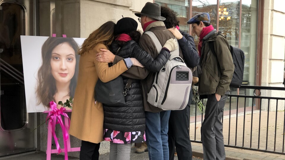 Des gens s'enlacent devant une photo de la victime.