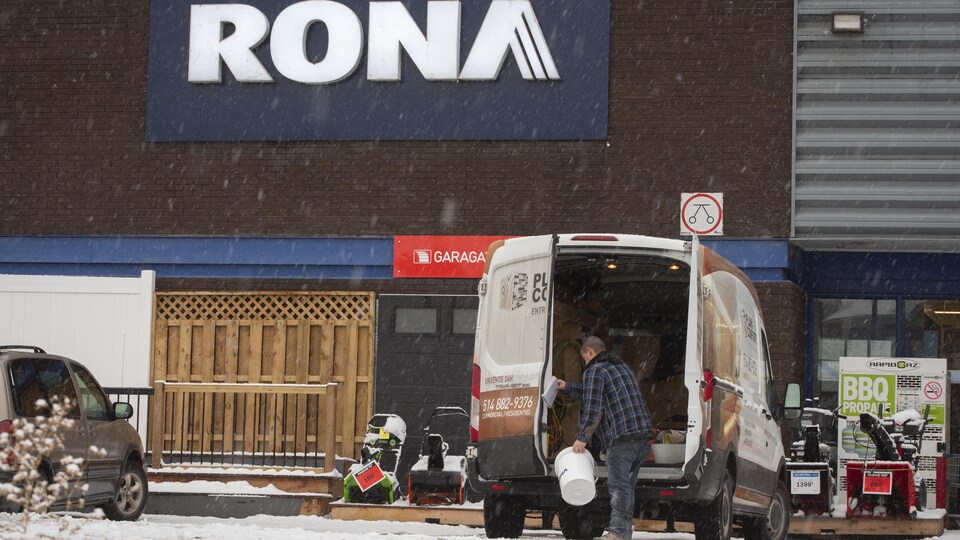 Un homme place des marchandises dans son camion, devant un Rona.