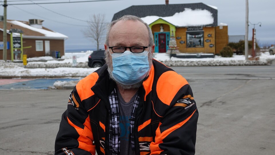 Ronald Michaud photographié avec un masque bleu devant un commerce de Carleton-sur-Mer.