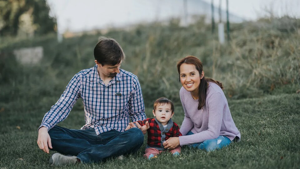 Ronna Sigua est assise dans un espace vert avec son enfant et son conjoint. 