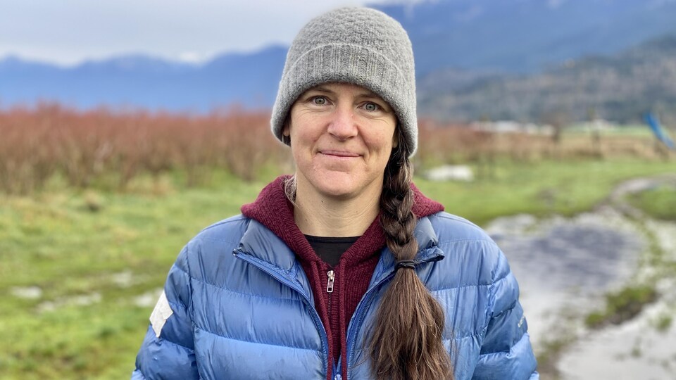 Une femme sourit, elle est devant un champ dans une ferme.