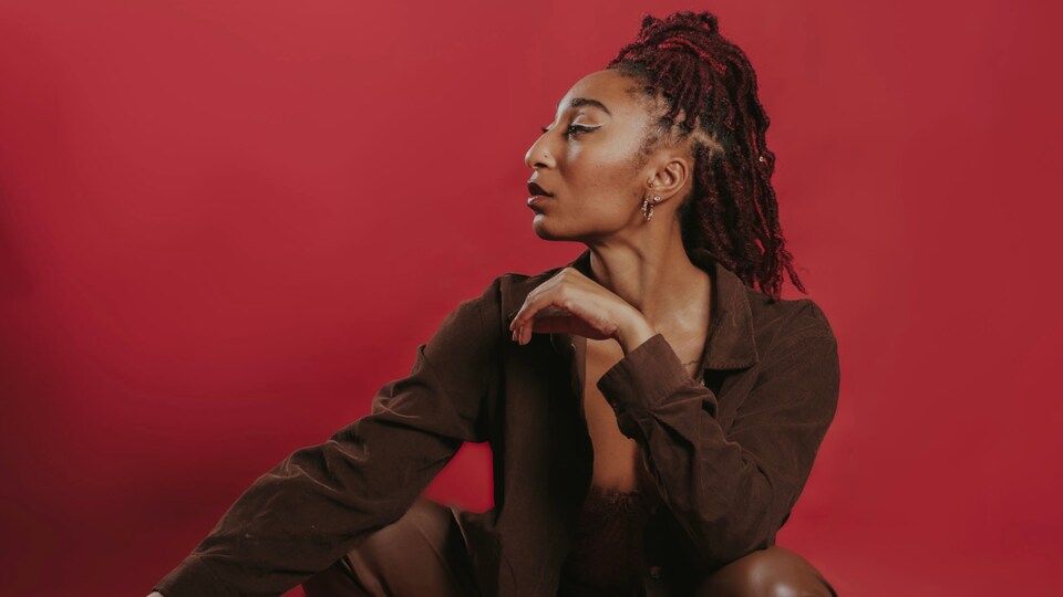Une femme en talons hauts en position assise devant un fond rouge.