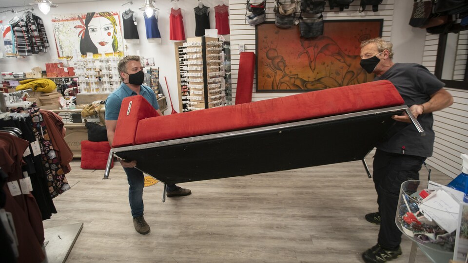 Deux hommes portant un masque transportent un canapé rouge.
