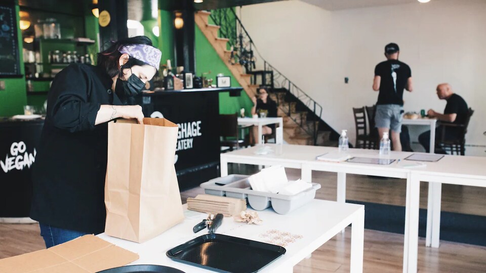 Une femme masquée prépare une commande à emporter dans la salle à manger d'un restaurant.