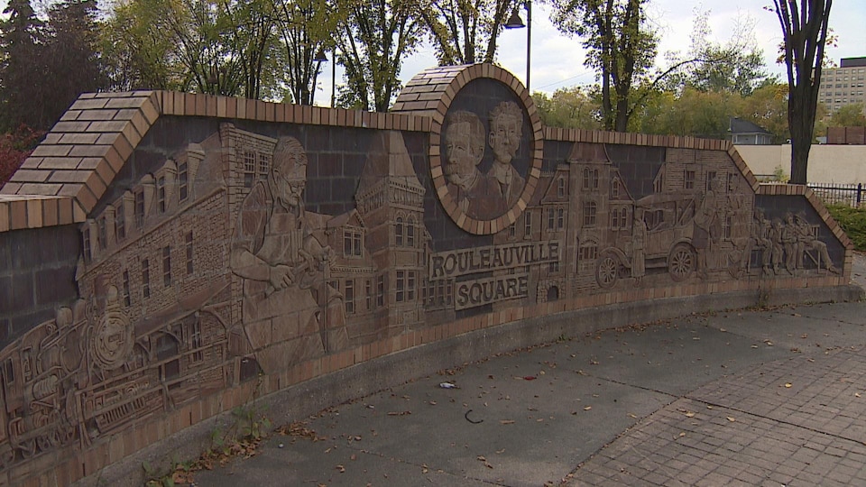 Vue sur un mur de brique rouge dans un parc. Sur le mur il est inscrit Rouleauville.