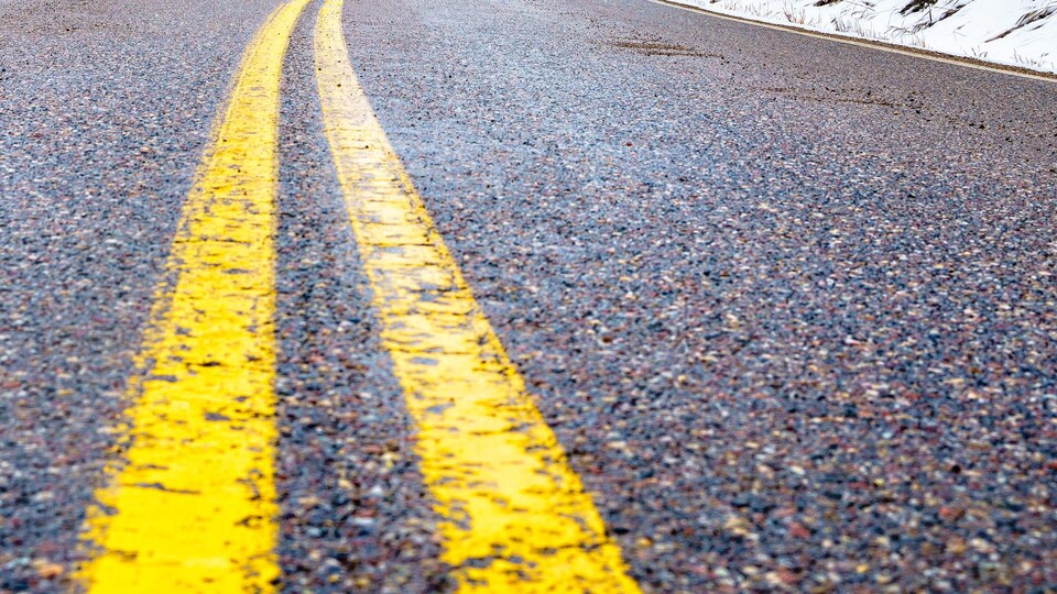 Plan rapproché des deux lignes jaunes parallèles peintes au milieu d'une route bordée d'une mince couche de neige.