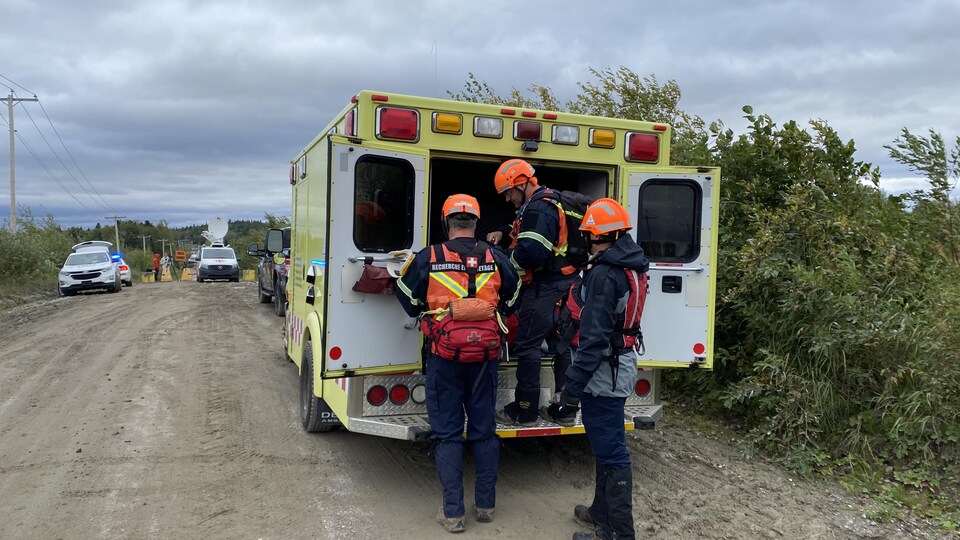 Des sauveteurs derrière une ambulance sur une route de gravier.