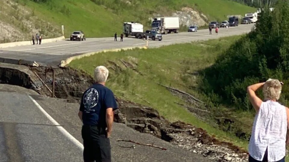 Des gens regardent le trou laissé par l'eau sur la route de l'Alaska.