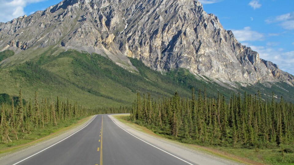 Une route dans la forêt et une grande montagne rocheuse en arrière-plan.