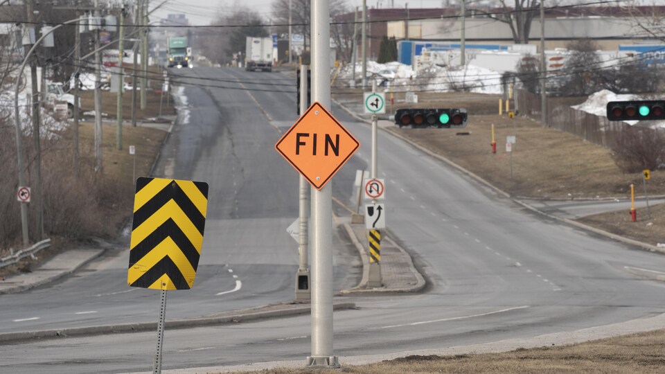 Une rue presque déserte dans un secteur industriel, avec au loin des camions.