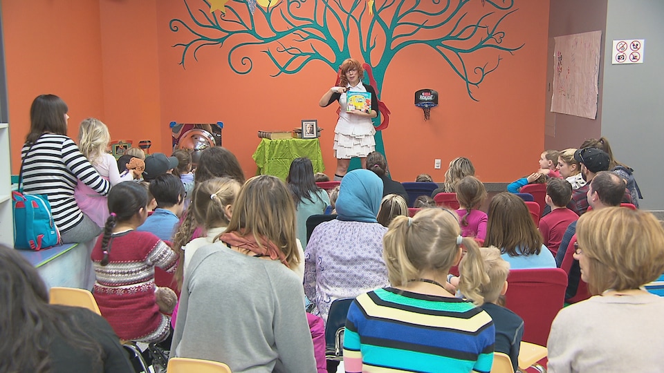Féeli Tout montre un livre à une petite foule d'enfants accompagnés de leurs parents