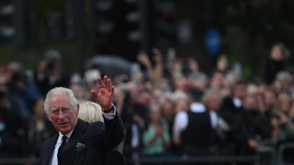 Le roi Charles III lève la main et salue la foule. 