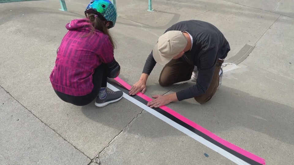 Une jeune adolescente et l'instructeur Matt Janz, accroupis, collent une bande adhésive rose fluo au sol. 