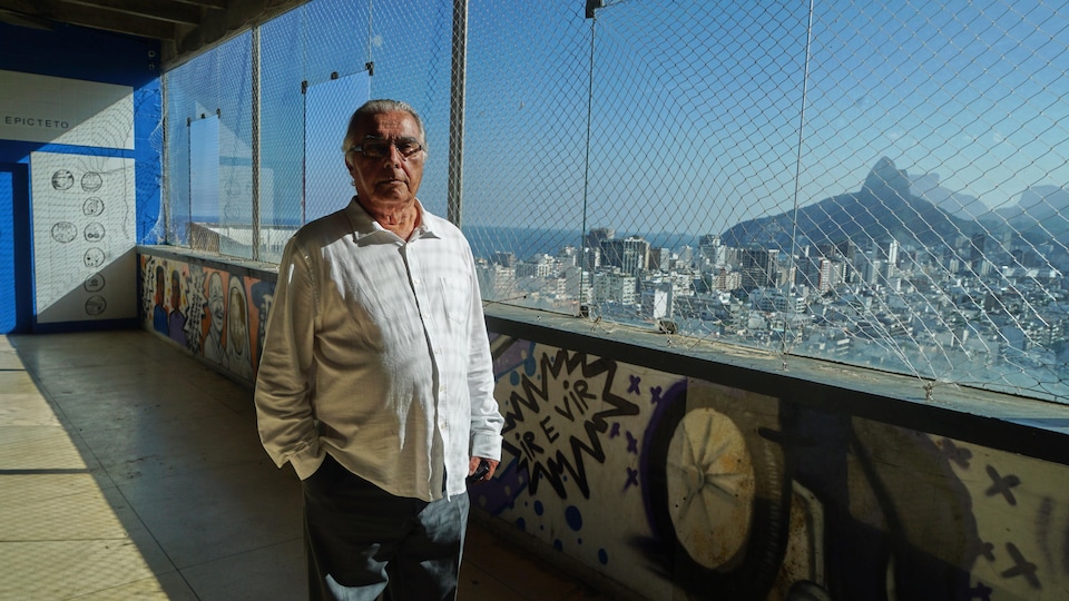 Rubem César Fernandes devant une fenêtre qui surplombe la ville de Rio de Janeiro, au Brésil.