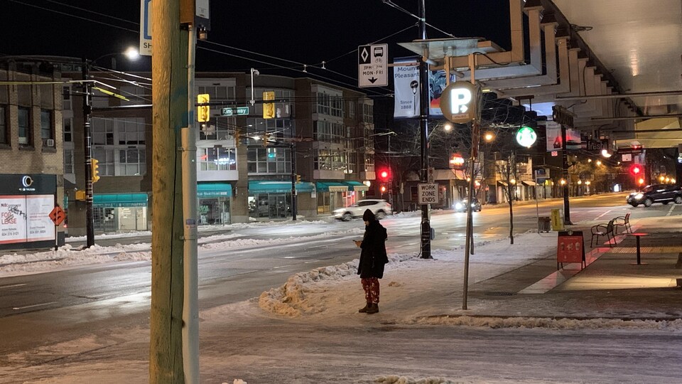Une personne sur un coin de rue enneigé de Vancouver. Les rues semblent glacées.