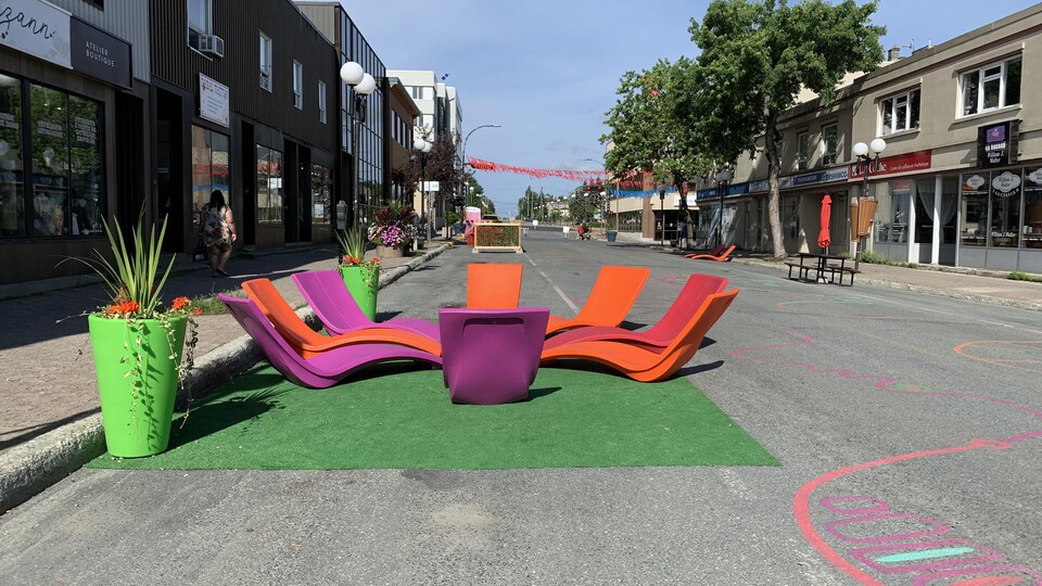 Des bancs colorés installés dans la rue, avec des dessins sur l’asphalte et des banderoles au dessus du trottoir.