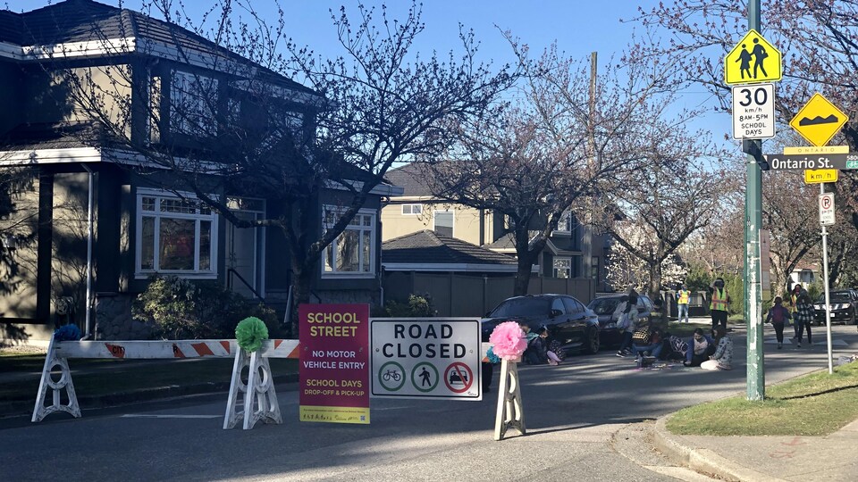 Des enfants dessinent sur la chaussée. Devant eux, une barricade où il est écrit : «rue fermée».