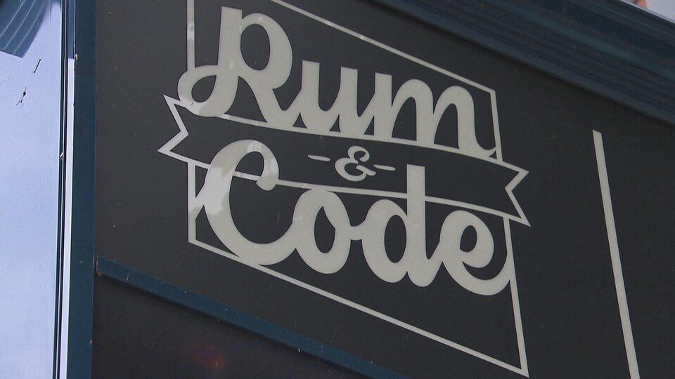 Sur un fond noir, à l'extérieur d'un édifice, on peut lire : Rum and Code.