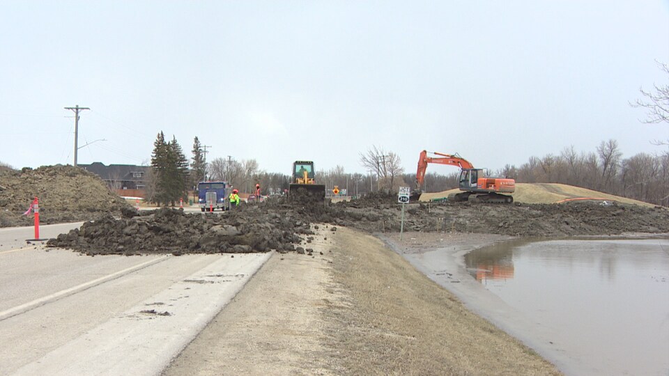 Des employés municipaux construisent une digue en terre le long d'une route.