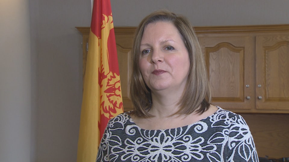 Jennifer Russell en entrevue devant un drapeau du Nouveau-Brunswick.