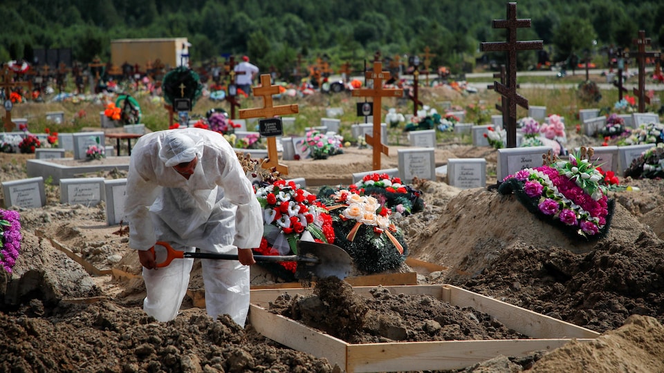 Un homme creuse une tombe, habillé d'équipement de protection personnel.
