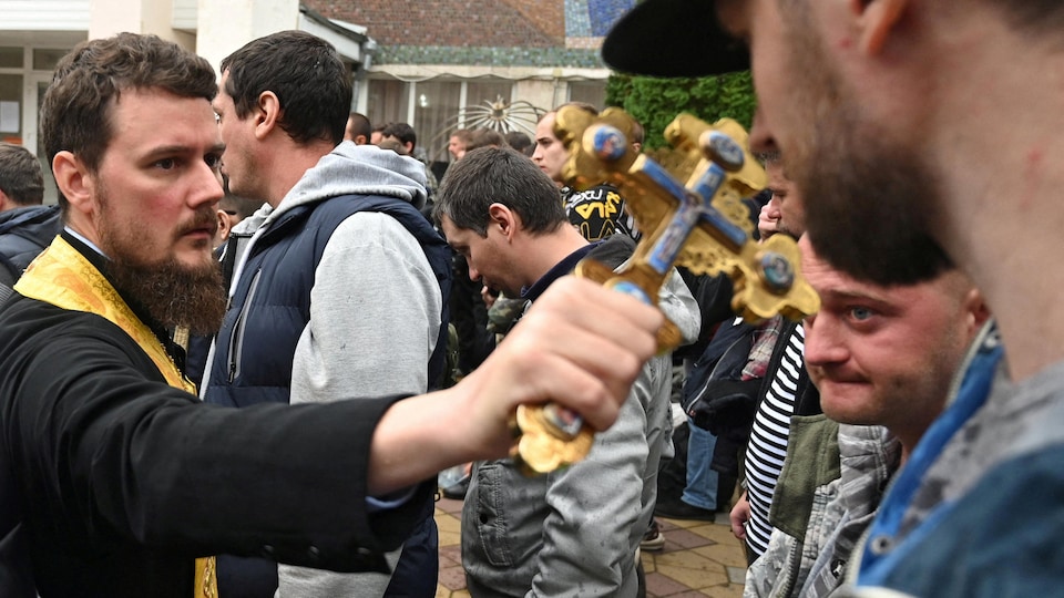 Un prêtre porte une croix au front d'un homme.