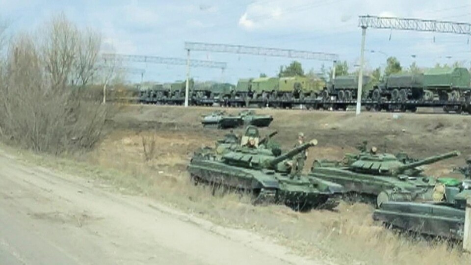 Des tanks sur le bas-côté de la route et, en arrière-plan, des véhicules militaires montés sur un train.