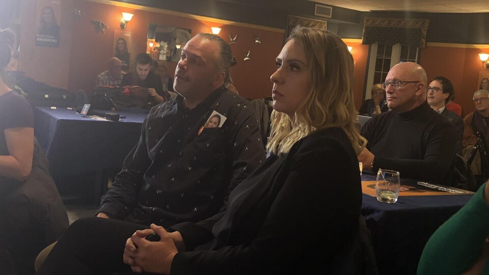 Ruth Ellen Brosseau avec son conjoint qui regarde au loin un écran.