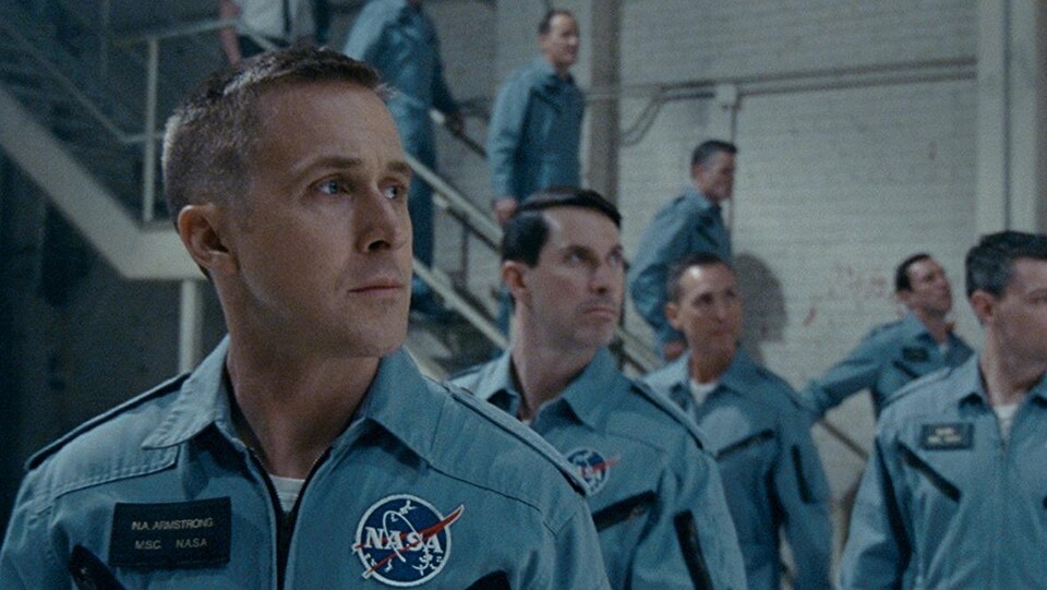 Ryan Gosling, en uniforme de la NASA, regarde vers la droite, tout comme d'autres astronautes derrière lui.