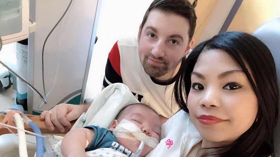 Ryan et Kristine avec un bébé dans les bras, dans une chambre d'hôpital. Le bébé a des tubes dans le nez et dans la bouche.