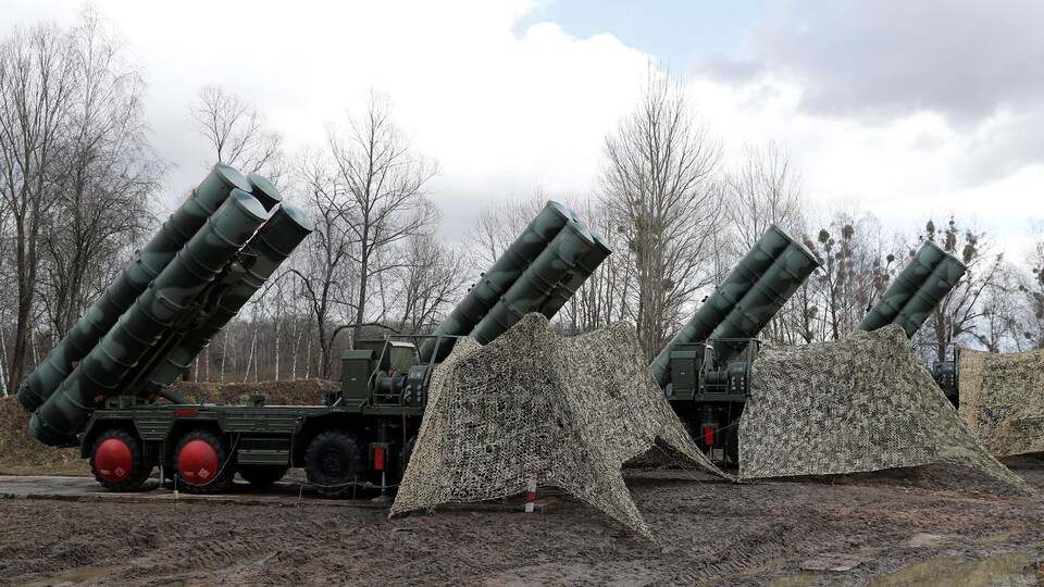 Quatre camions dont la cabine est recouverte d'un filet de camouflage déploient des tubes lance-missiles contenant des missiles S-400 russes. 