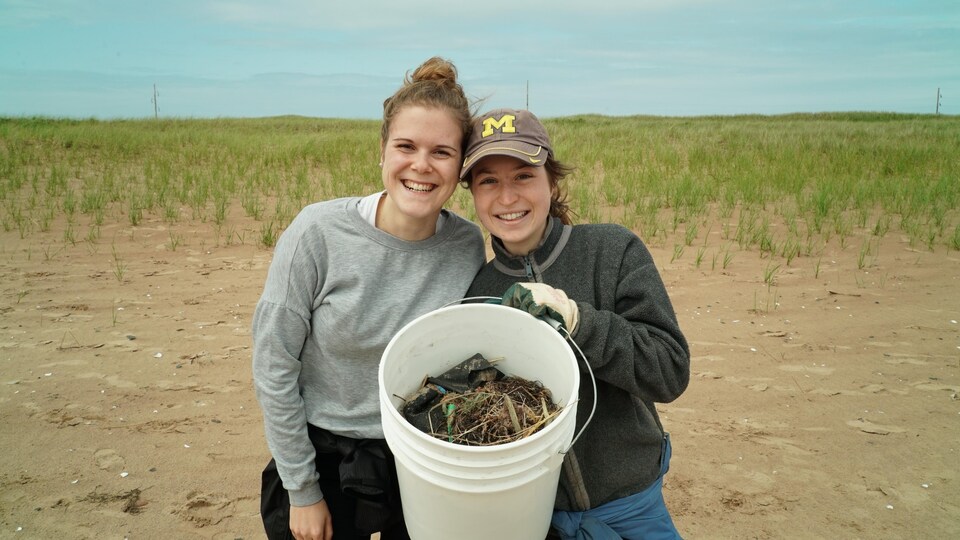 Sabrina Chiasson et Édith Turbide sourient en montrant le contenu d'un seau rempli de déchets.