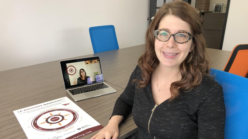 Sabrina Dion est assise à une grande table devant un ordinateur portable et une affiche de la boussole marketing.