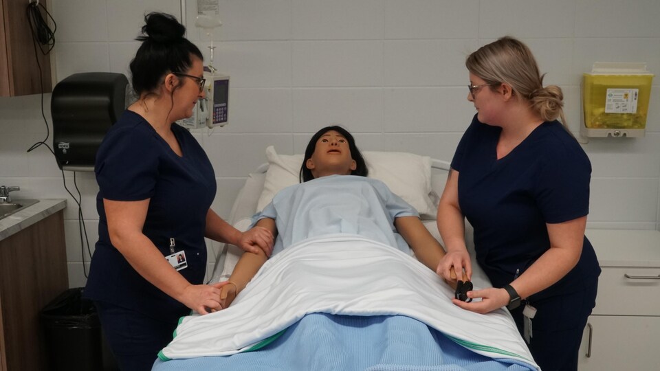 Deux femmes se trouvent de chaque côté d'un mannequin intelligent couché dans un lit d'hôpital.