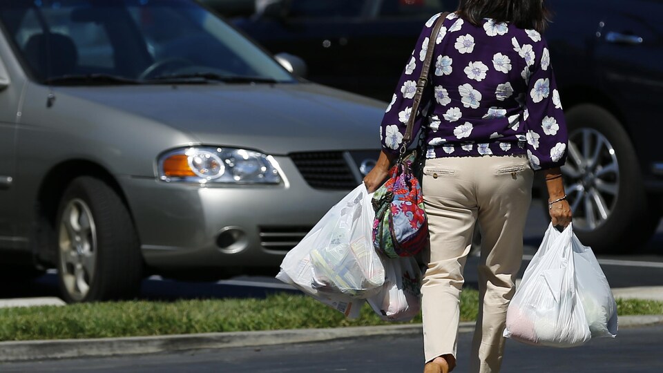 Une dame marche en tenant quatre sacs de plastique.