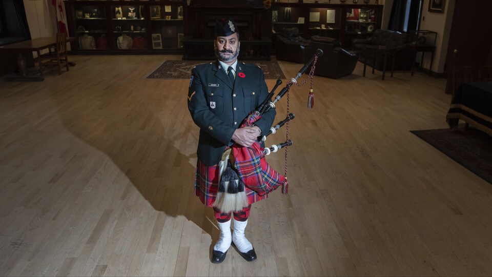 Un homme en uniforme pose dans le salon régimentaire du Black Watch à Montréal, sa cornemuse sous le bras.