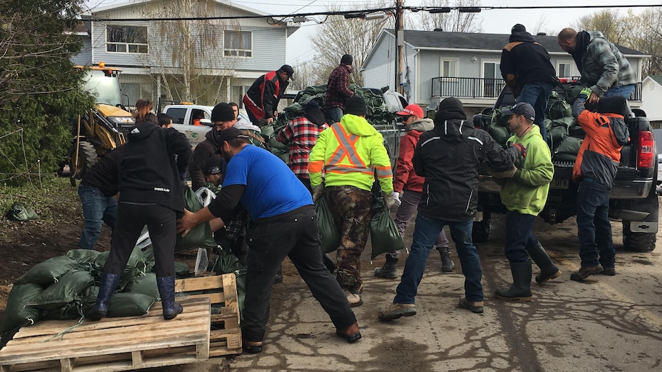 Des hommes sortent des sacs de sable de camionnettes
