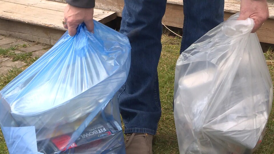 Un homme tient un sac de recyclage et un sac à ordures.
