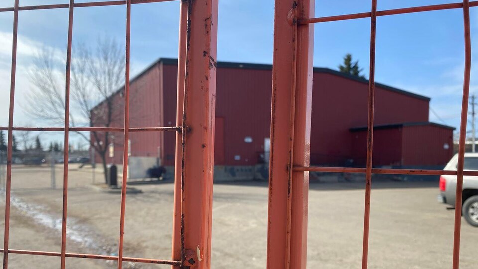 Un bâtiment carré rouge vu à travers une clôture.